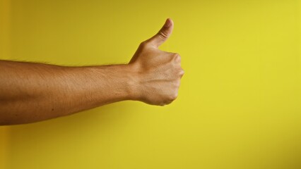 Man's hand giving a thumbs up against a vibrant yellow background with visible fingers and arm hair.