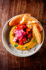 bowl of creamy hummus garnished with red onions, cherry tomatoes, and fresh herbs, served with pita bread on side. Perfect for culinary themes, Mediterranean cuisine, and healthy eating concepts.