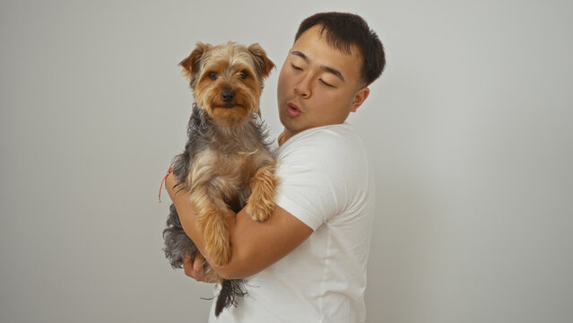 A young asian man from china holds his dog over a white background wall, both looking content and connected in this isolated pet portrait.