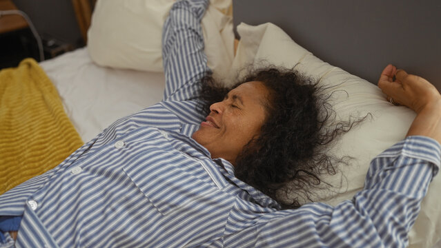 Woman stretching in bed wearing pajamas in a cozy bedroom with a comfortable pillow and soft blanket, enjoying a relaxed morning at home