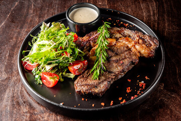 Grilled steak on a black plate with a side salad and sauce. Perfect for culinary, food photography, or restaurant menu content. High-quality image showcasing delicious, well-prepared cuisine.