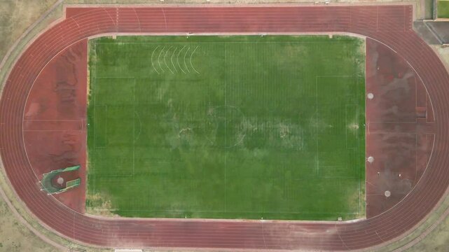 An aerial slowly zooming in of a weathered track and field or athletics field with a dusty exterior