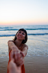 Follow me. happy young woman pulls guy's hand. a beautiful girl in a dress walks along the beach, holding a guy?s hand, a romantic walk.