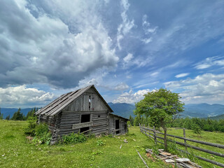 Wooden old hut against green mountains and dramatic sky.