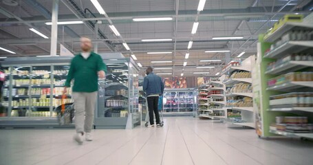Group of Shoppers Walking in a Busy Modern Supermarket, Selecting Food Products from Well Stocked Shelves. People Browsing Fresh Produce and Essentials. Footage with Fast Forward Effect