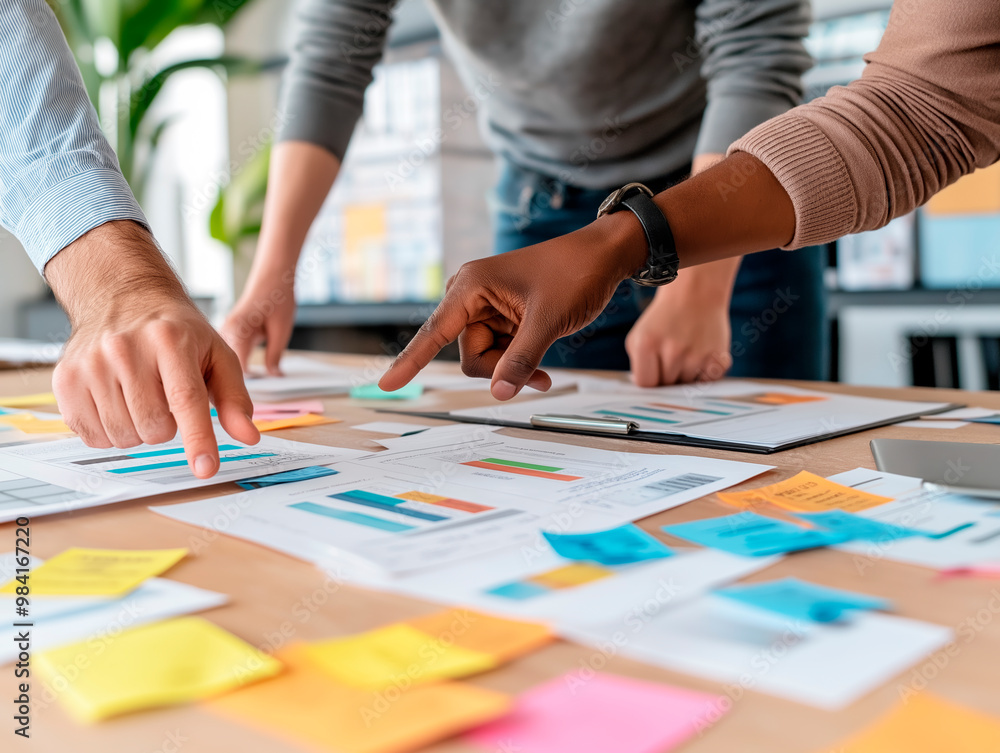 Poster team members brainstorming with documents and sticky notes on a wooden table in a modern office.