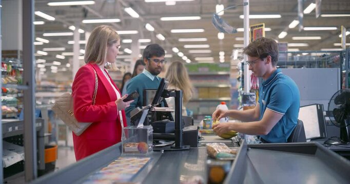 Portrait of a Male Cashier in a Blue Shirt Efficiently Scanning Groceries for Diverse Customers at a Busy Supermarket Checkout, Ensuring a Smooth and Quick Shopping Experience