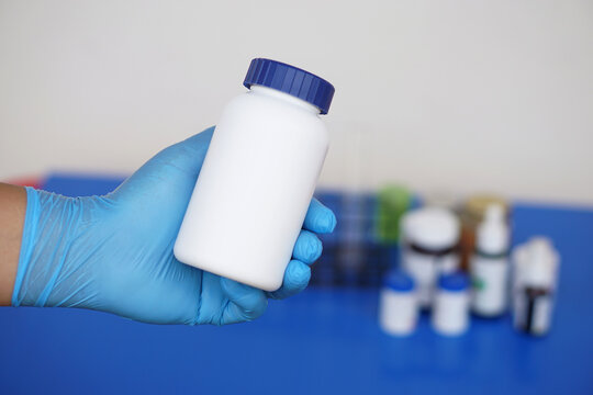 Chemist's hand wears protective glove, hold white bottle of chemicals or medicine. Concept,chemical substance industry manufacturing pharmacy. Scientific experiment in chemistry laboratory.