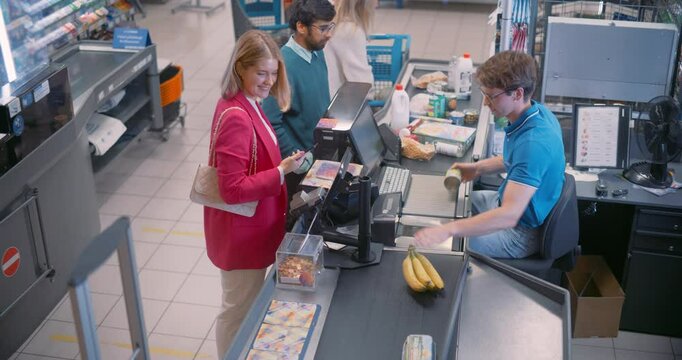 Male Cashier Scans Groceries at the Checkout Counter, His Hands Swiftly Moving as He Registers Each Item. He Engages with Female Customer while Ensuring a Quick and Accurate Transaction