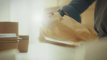 An employee of mobile coffee shop, working on bright sunny day, carefully packs freshly baked croissants in environmentally friendly paper packaging. Keeping a close eye on sustainable business trends