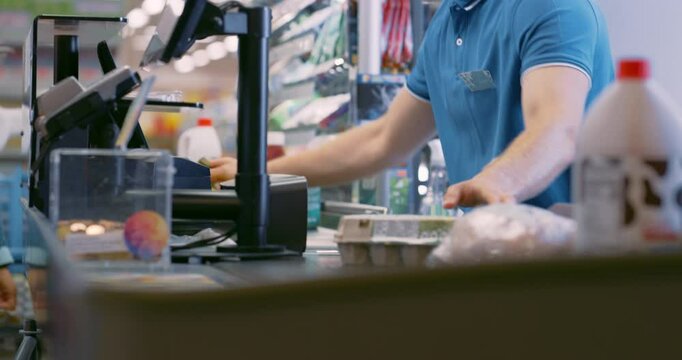 Male Cashier Scanning Product Items for Diverse Customers at a Busy Supermarket Checkout. Meat, Bananas, Eggs, Milk are Processed Efficiently, Groceries Rolling Down the Conveyor Belt