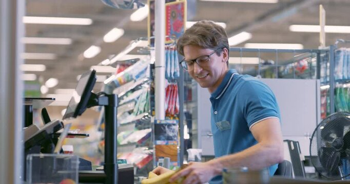 Portrait of a Male Cashier in a Blue Shirt Efficiently Scanning Groceries for Diverse Customers at a Busy Supermarket Checkout, Ensuring a Smooth and Quick Shopping Experience