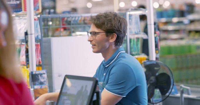 Young Cashier Working at a Supermarket Checkout. Worker Scanning Groceries for Customers at a Store Counter. Customers Waiting Patiently as the Cashier Processes the Items and Prepares the Bill