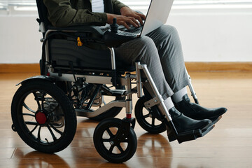 Obraz premium Close-up of man with disability sitting in wheelchair and typing on laptop
