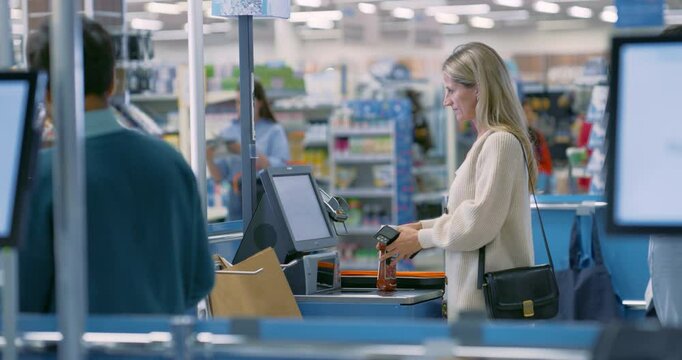 Female Shopper Using a Self-Service Checkout in a Modern Supermarket, Scanning Her Groceries One by One. Woman Pays Using Her Smartphone for a Contactless Payment