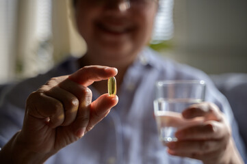 Close up hand of an elderly Asian woman is pouring vitamins from a bottle to take for boosting her immune system and nourishing her body. Senior people health care vitamin product concept.