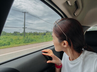 Naklejka premium Happy asian Thai woman sitting at back as passenger while traveling by car on road in Thailand, looking out side the window.