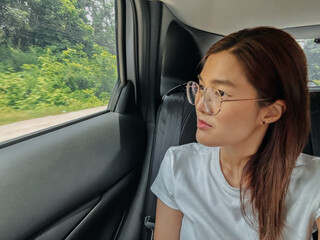 Naklejka premium Happy asian Thai woman sitting at back as passenger while traveling by car on road in Thailand, looking out side the window.