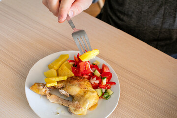 A person eating a healthy meal with roasted chicken, pineapple, and vegetable salad, focusing on balanced diet and nutrition