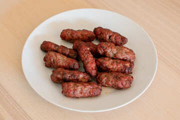 Grilled Romanian mici sausages on a white plate, perfect for barbecue gatherings and traditional holiday celebrations like Easter