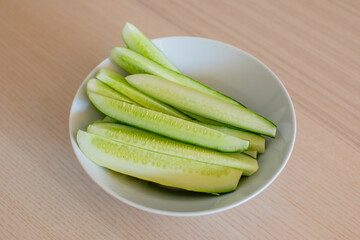 Freshly sliced cucumbers in a white bowl on a wooden table, ideal for healthy eating and summer salad recipes