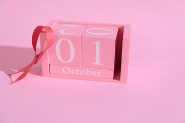 Pink calendar block displaying October 1st with a folded ribbon on a soft pink background,...