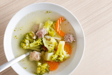 A bowl of nutritious homemade vegetable and meatball soup on a wooden table, perfect for comforting winter meals