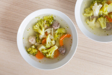 White bowls of homemade vegetable and meatball soup, perfect for warming up during cold winter days or holidays