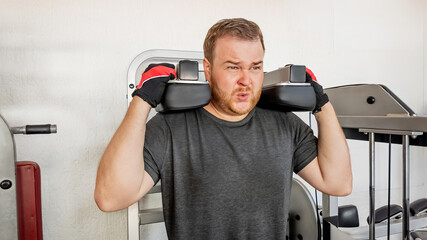 A Caucasian man struggles while lifting weights in a gym, illustrating the challenges of...