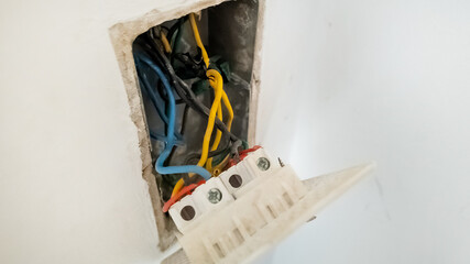 An exposed electrical wiring box revealing blue, yellow, and black wires, highlighting home maintenance and electrical safety hazards