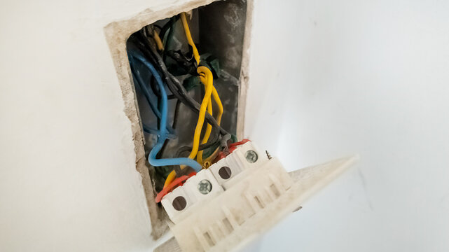 An exposed electrical wiring box revealing blue, yellow, and black wires, highlighting home maintenance and electrical safety hazards