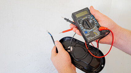 Person using a digital multimeter to check electrical wiring for repairs, demonstrating home...