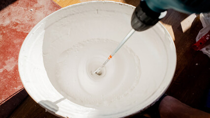 Mixing white paint with an electric drill in a bucket for house renovation projects