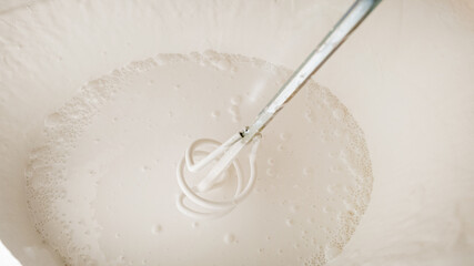 Close-up view of a whisk stirring a bowl of pancake batter, concept of breakfast preparation or...