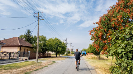 Obraz premium A Caucasian man rides a bicycle through a quaint rural village street during a sunny summer day, highlighting the importance of outdoor exercise