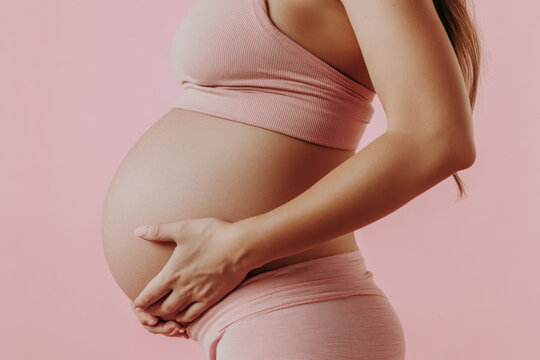 Close up side view of pregnant young expecting woman round belly pink background. Maternity concept