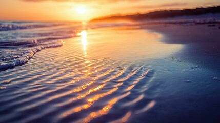 Close-up shot of the golden sun reflecting off the water's surface on a sandy beach.