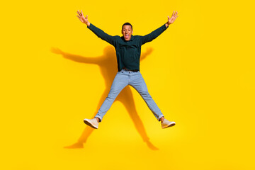 Fototapeta premium Full length photo of attractive young man jump star pose spread arms legs dressed stylish green clothes isolated on yellow color background