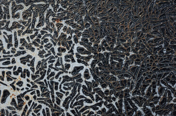 Intricate pattern of peeling and swollen black paint exposing white and rust on old metal surface...