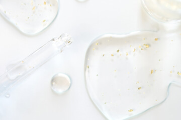 Transparent serum with gold particles and dropper on white surface for luxury skincare and beauty treatments.