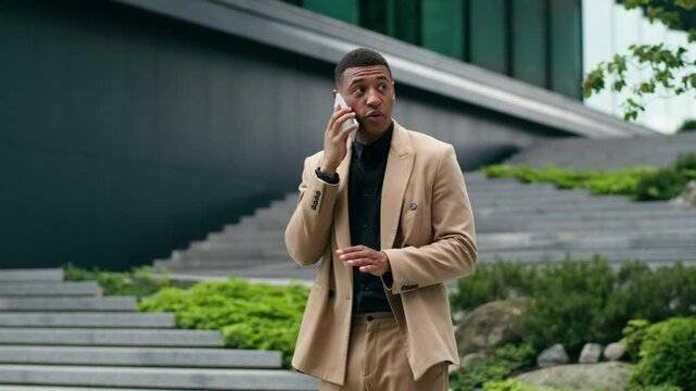 Confident African American ethnic businessman man business guy male leader investor real estate trader employer entrepreneur in city talking mobile phone call smartphone problem stress conversation