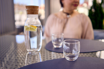 a plus size woman in peach fuzz dress chooses a dish in a restaurant via QR code in smartphone, water with lemon and glasses in front of her