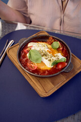 medium sized woman in peach fuzz dress eating Shakshouka in modern restaurant