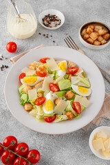 Caesar salad with lettuce, grilled chicken breast, boiled eggs, tomatoes, parmesan cheese and croutons in a ceramic plate on a concrete background. Top view.