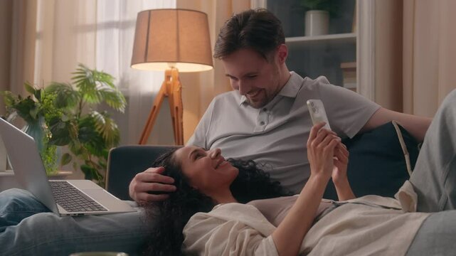 Gadget addict family internet addiction couple Caucasian man freelancer guy male using laptop computer Hispanic woman user Latina girl lady together use mobile phone smartphone at home couch relaxing