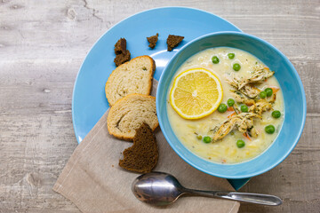 Food Cuisine Concepts. Italian Lemon Chicken Orzo Delicious Soup in Blue Bowl With Loafs of Dark and White Bread With Spoon Over Wooden Grey Background.