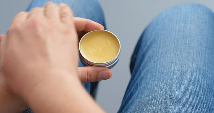 Woman applying balm to her index finger from a tin can and putting the balm on other hand