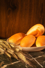 Food Ideas. Freshly Baked Home Bread Buns As Fresh Loafs of Bread on White Plate with Rye and Wheat Over Grunge Rustic Background As Crunchy French Baguettes.