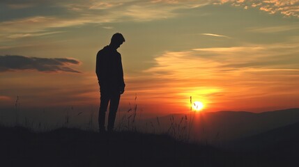 Obraz premium A silhouette of a sad man standing on a hill, with the sun setting in the background, casting a long shadow