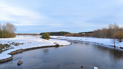 The canal with concrete banks flows among forested areas towards the city buildings. In winter...